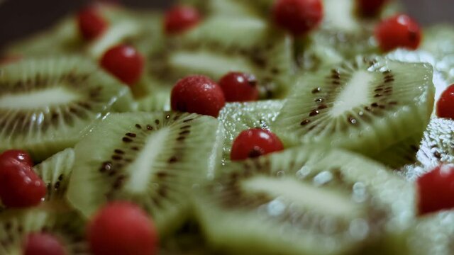 Juicy fresh kiwi slices and frozen red currant arranged in a shape of Christmas tree on a black marble cutting board. Food for Christmas holiday. Healthy snack. Macro view. Slowmotion