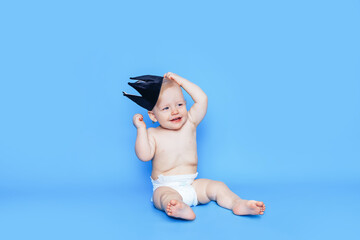 Little boy sits in front of a blue background. On the head is a black crown