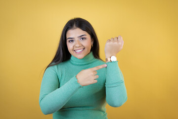 Young caucasian woman over isolated yellow background smiling, showing the watch and pointing