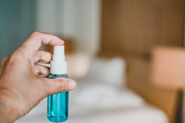 blue alcohol spray bottle in human's hand with blurred bedroom background