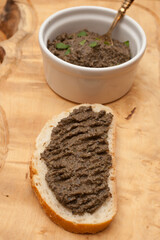 A tapenade spread on a piece of bread, served on a wooden platter