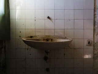 Detail from messy interior of abandoned building. Empty room with old dirty sink, cobweb and wall tiles.