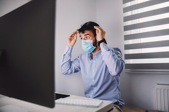 Young dedicated focused businessman with face mask on sitting in his office during corona virus outbreak and looking at computer.
