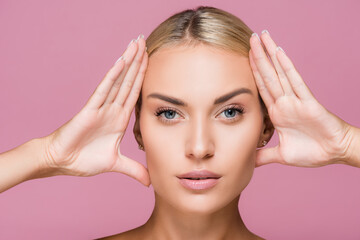 Naklejka premium beautiful blonde woman with perfect skin touching face isolated on pink