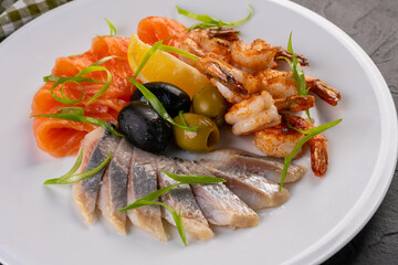 Seafood plate. seafood with olives and lemon on a white plate. grilled salmon, herring and tiger prawns with herbs and spices.