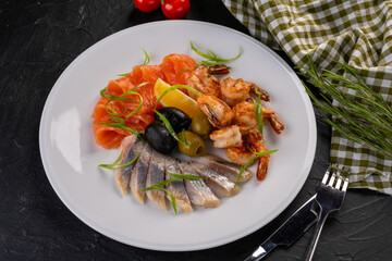 Seafood plate. seafood with olives and lemon on a white plate. grilled salmon, herring and tiger prawns with herbs and spices.