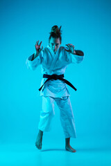 Obraz premium Attack. Professional female judoist in white judo kimono practicing and training isolated on blue neoned studio background. Grace of motion and action. Healthy lifestyle, sport concept