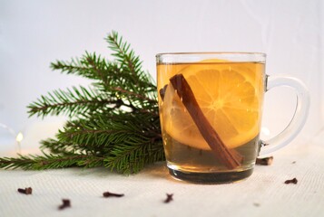 Hot winter flavored drink. Glass mug with tea, orange and cinnamon on the window. Green branches of the Christmas tree