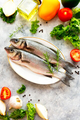 Seabass fish with fresh vegetables on gray textured background, top view.