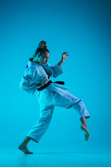 Fototapeta na wymiar Active training. Professional female judoist in white judo kimono practicing and training isolated on blue neoned studio background. Grace of motion and action. Healthy lifestyle, sport concept