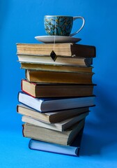 a stack of books on which stands a tea mug with a tea bag, blue background