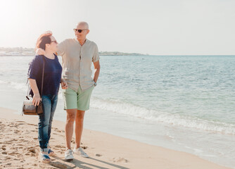 Middle-aged couple walking by the sea - retirees enjoy their free time walking in nature - warm filter on background