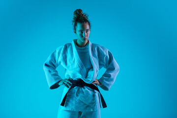 Posing. Professional female judoist in white judo kimono practicing and training isolated on blue neoned studio background. Grace of motion and action. Healthy lifestyle, sport and movement concept