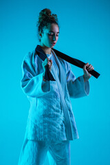 Take a rest. Professional female judoist in white judo kimono practicing and training isolated on blue neoned studio background. Grace of motion and action. Healthy lifestyle, sport concept