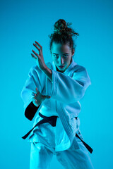 Attack. Professional female judoist in white judo kimono practicing and training isolated on blue...