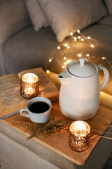Still life teapot, book, cup of coffee, candles in the living room on a wooden table. Cozy interior concept