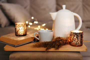 Still life teapot, book, cup of coffee, candles in the living room on a wooden table. Cozy interior concept