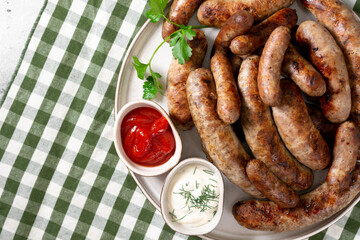 Fried sausages. Bavarian and Nuremberg sausages with spices, sauce, tomatoes and parsley. Delicious meat sausages in a white ceramic plate on a light gray table. German dish