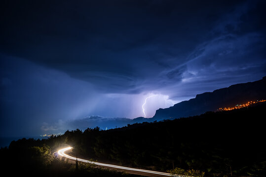 Thunderstorm over the mountains of the southern coast of Crimea with white traces of car headlights in the foreground