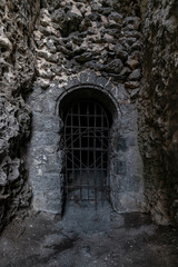 Fototapeta premium The entrance to a dark dungeon in the mountain, closed by a rusty metal grating