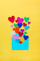 Paper envelope full of colorful paper hearts on yellow background. Concept of love.