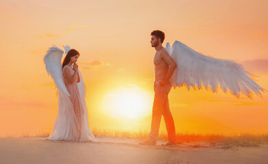 artistic processing. Two divine angels man and woman go to meet each other. design white costume wings. Girl with loose long hair brunette. Backdrop bright sunny sunset in fabulous natural sand desert