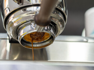 making coffee in a professional coffee machine from an open holder. espresso. Espresso preparation, extraction process. Bottom view of the coffee machine.  a thin trickle of coffee pours into the Cup