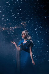 Fototapeta na wymiar Young beautiful woman queen. blonde girl with fantasy mystic dragon. Carnival fairy tale character costume medieval dress style. Halloween image. Backdrop night winter blue snow fall blizzard