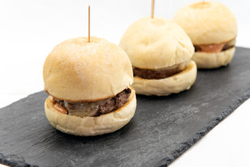 Authentic Italian food shows three cheeseburger sliders served on a slate plate and ready to eat.