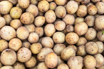 Langsat tropical fruit pile on farm market. Fruit season in South Asia. Farm market in Thailand or Vietnam. Tasty exotic fruit texture for package design. Lanzones bunch closeup. Small yellow fruit
