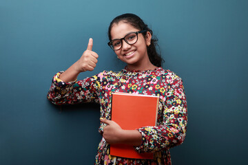 Smiling girl holding note books in her hand shows thumbs up gesture