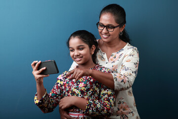 Happy mother and daughter of Indian ethnicity looking at the mobile phone