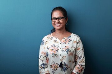 Portrait of a smiling woman of Indian ethnicity against a blue wall