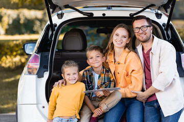 Fototapeta na wymiar Cheerful family with map looking at camera near trunk of car outdoors