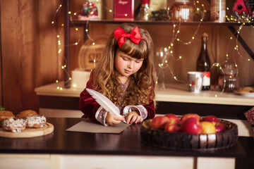 Little girl writes a letter to Santa Claus. A child near the Christmas tree. Happy child smiles. Girl with long curly hair