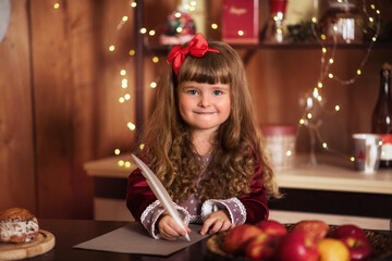 girl with cake. Little girl writes a letter to Santa Claus. A child near the Christmas tree. Happy child smiles. Girl with long curly hair