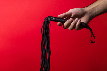 Leather whip. A man's hand holds a leather whip on a red background. BDSM accessories