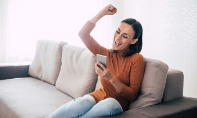 Fototapeta premium Happy excited beautiful woman with smart phone on the couch
