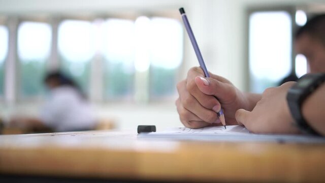 Hand Student use pencil writing on paper optical form of standardized test examination, Answer sheet, doing final exam attending in examination classroom