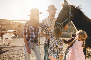 Happy family with horse having fun at farm ranch - Parentc and children cuddling animal pet at...