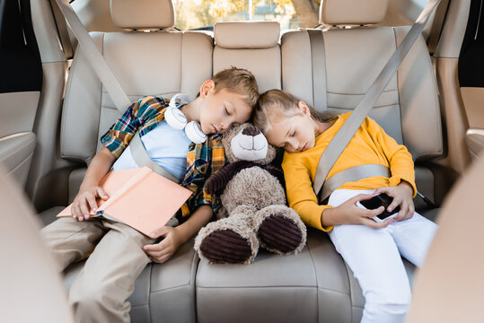 Kids with smartphone, book and soft toy sleeping in auto during travel