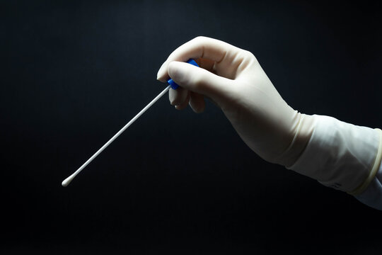 Doctor's Hand With White Sterile Gloves Holds PCR Test For Covid-19 In Profile, Black Background