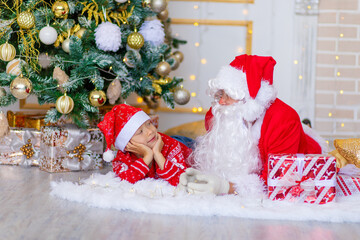 Fototapeta premium child and Santa Claus near the Christmas tree, boy looks at Santa Claus