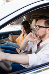 Pensive man driving car near wife with coffee to go and map on blurred background