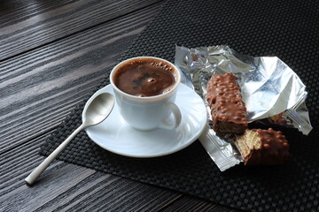 White cup with coffee and waffles in chocolate on a dark background
