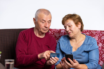 An elderly couple pays online with a bank card using a cellphone. Pandemic and online concept.