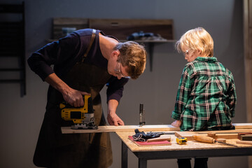 an experienced carpenter shows the work of various tools to his son in the workshop