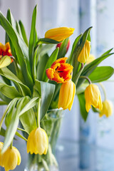 A bouquet of red and yellow tulips stands in a glass vase on the table. Vertical image. Selective focus, blurred background.