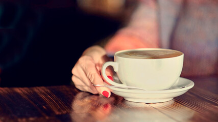 woman hands with latte on a wood table. woman with red nails holds coffee in her hands.