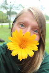 A female with a big yellow sunflower in her mouth outdoors.
